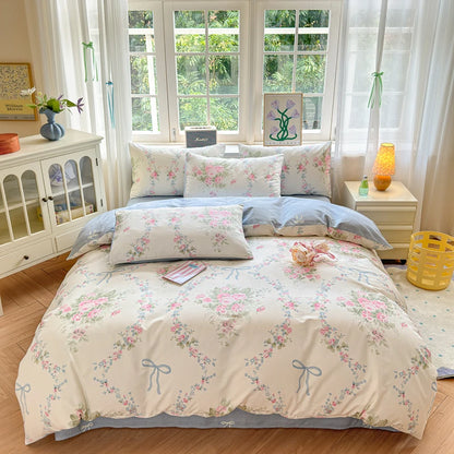 A 100% Cotton Rose & Ribbon Duvet Cover Set displayed in a bedroom setting, featuring a pattern of pink roses and blue bows on a cream background.