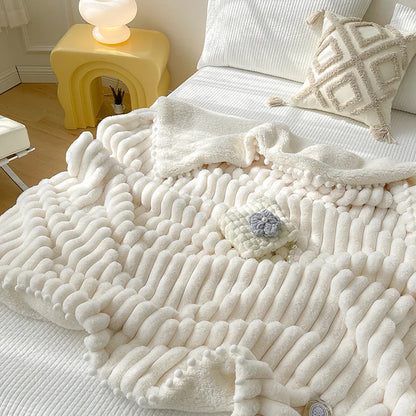 A plush bed throw in white, cream, and pink colours, featuring a ribbed design with a pom pom trim