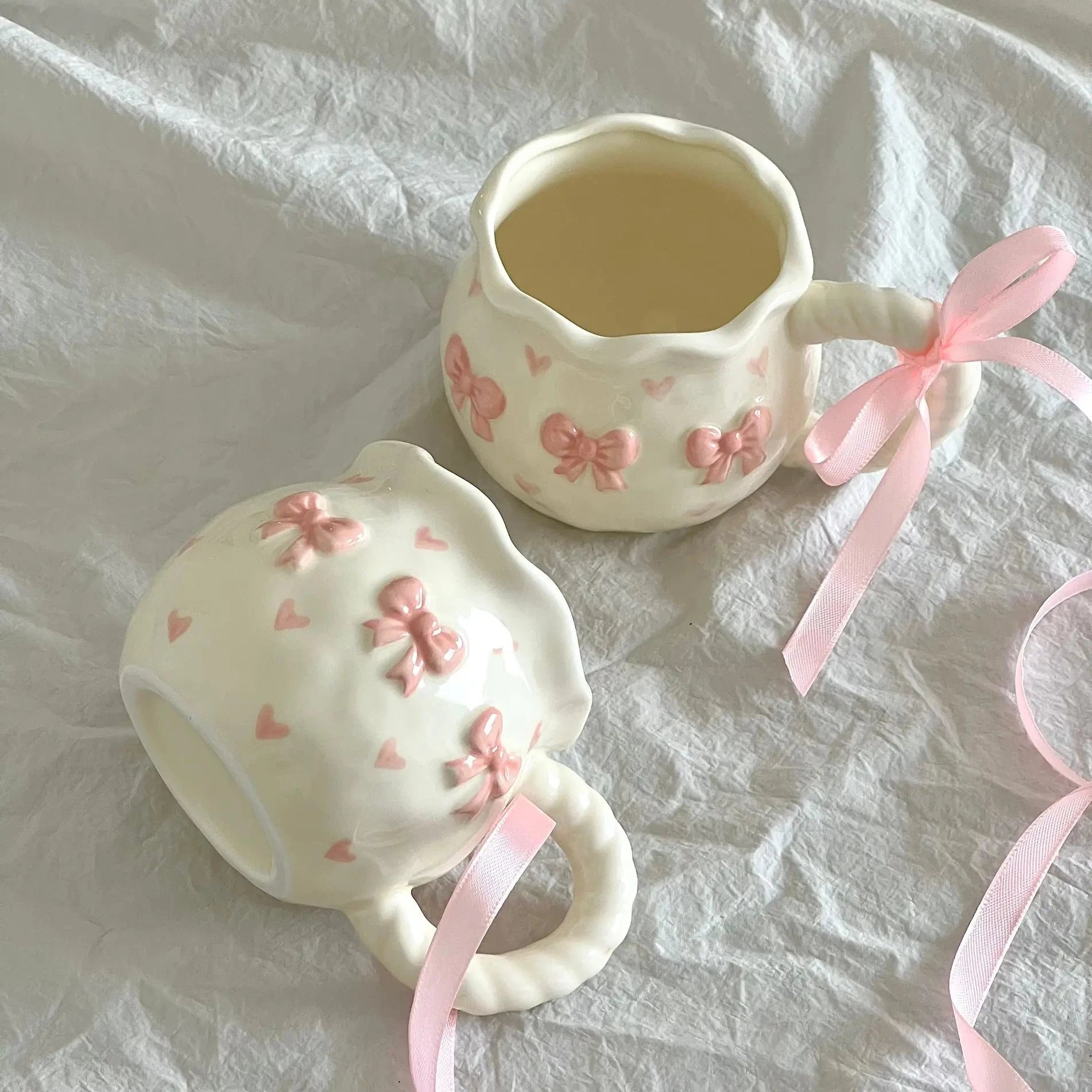 Two ceramic teacups with pink floral designs and ribbons 